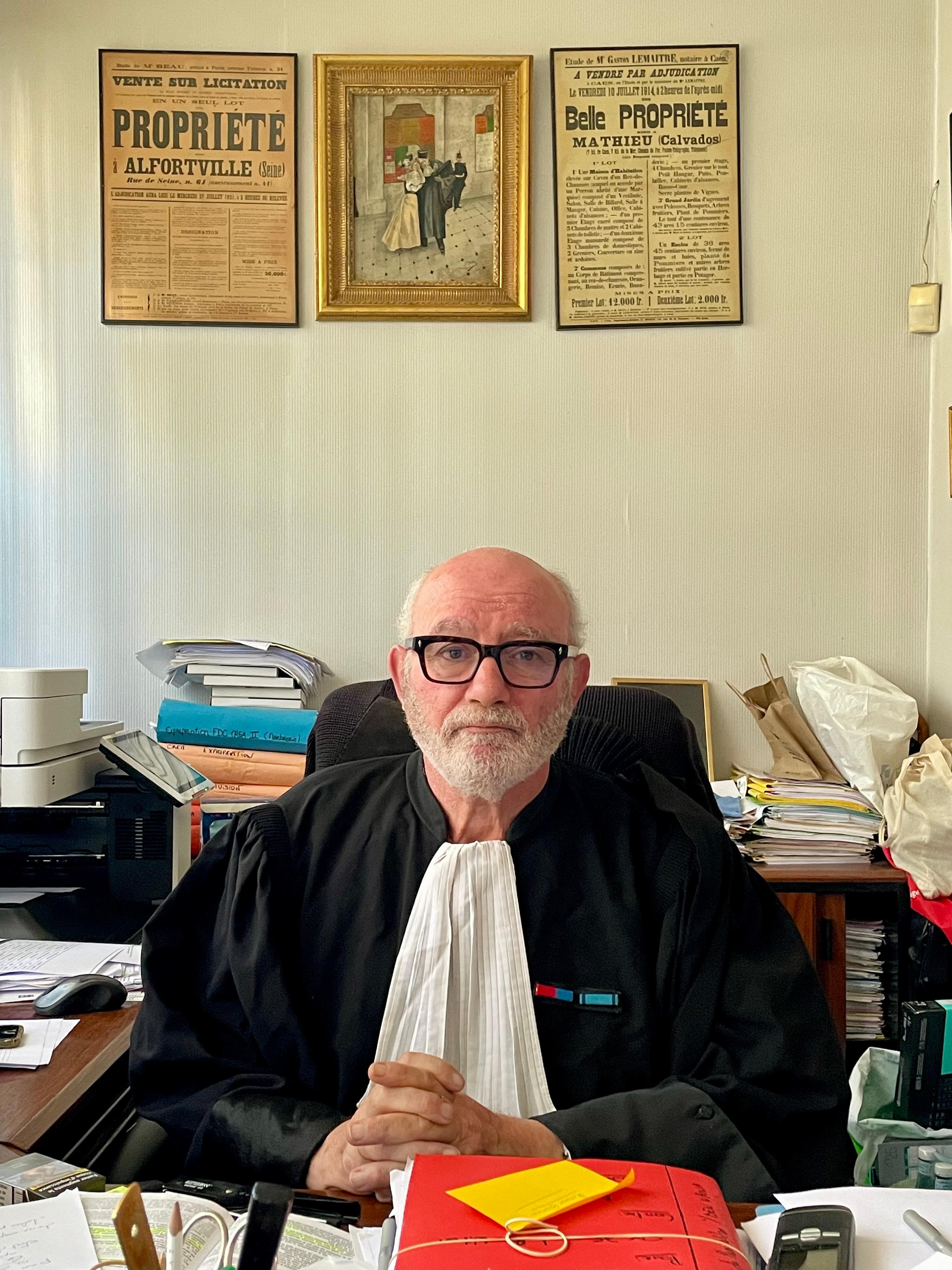 Maître Guibère en robe d'avocat, dans son cabinet devant des affiches historiques de ventes immobilières